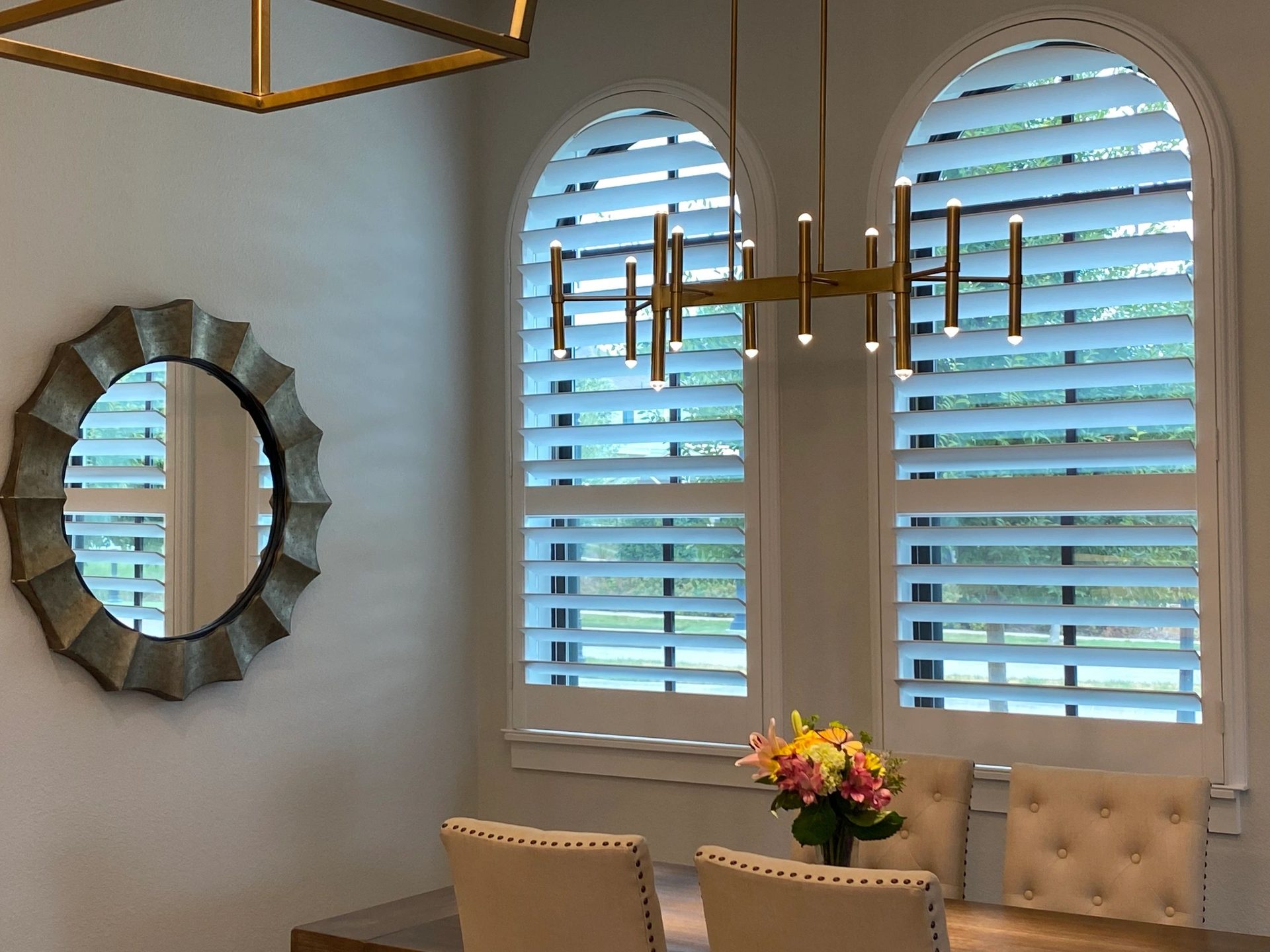 Arched custom shutters in a dining nook with brass chandelier and sunburst mirror